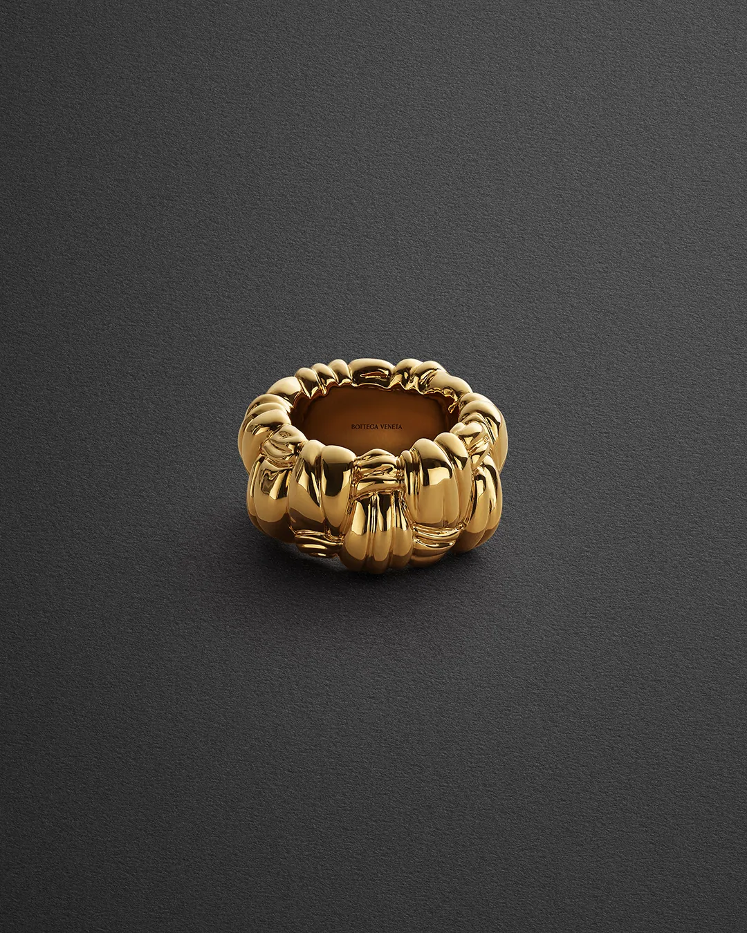 Bottega Veneta gold statement ring with polished sculptural detailing on dark textured background