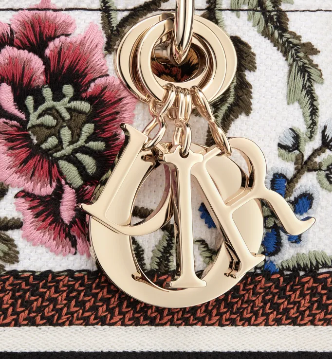 Detailed view of Dior bag with floral embroidered fabric and gold Dior logo charm in portfolio image